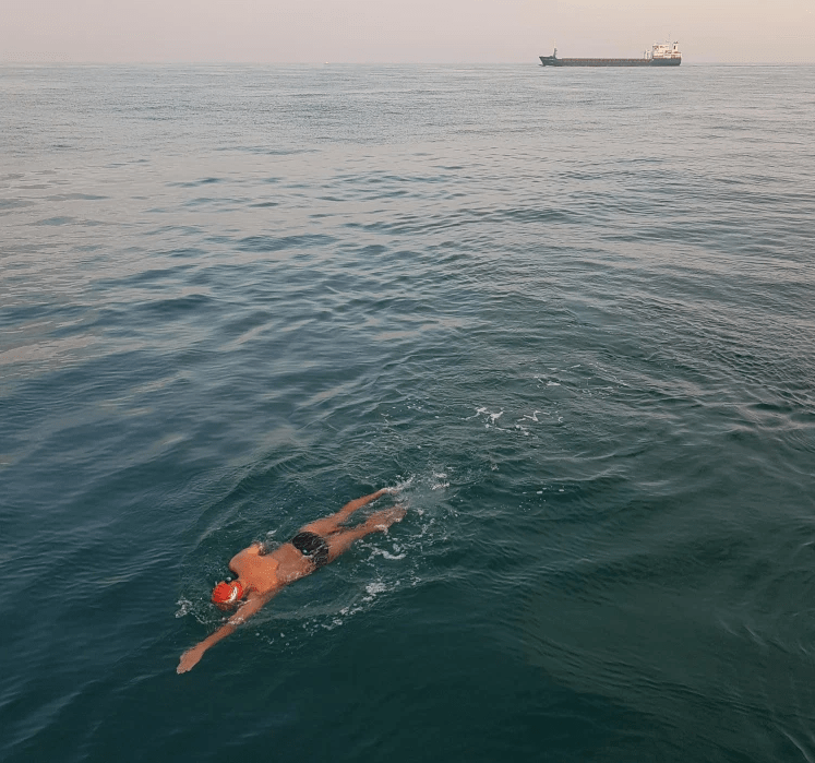 Man swimming in English Channel with shipping tanker in background